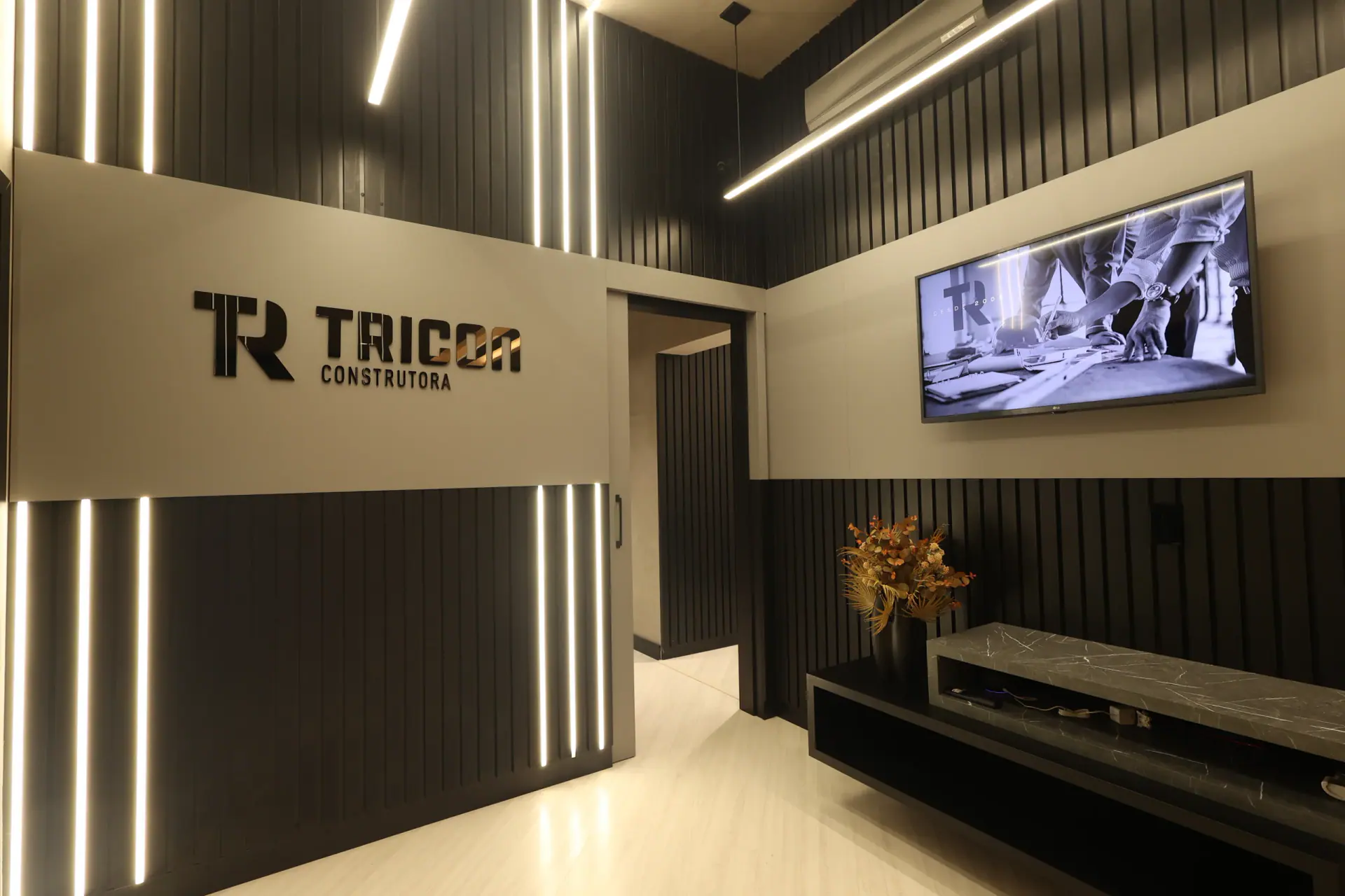 Recepção da sede Tricon, com marca na parede e área de espera
