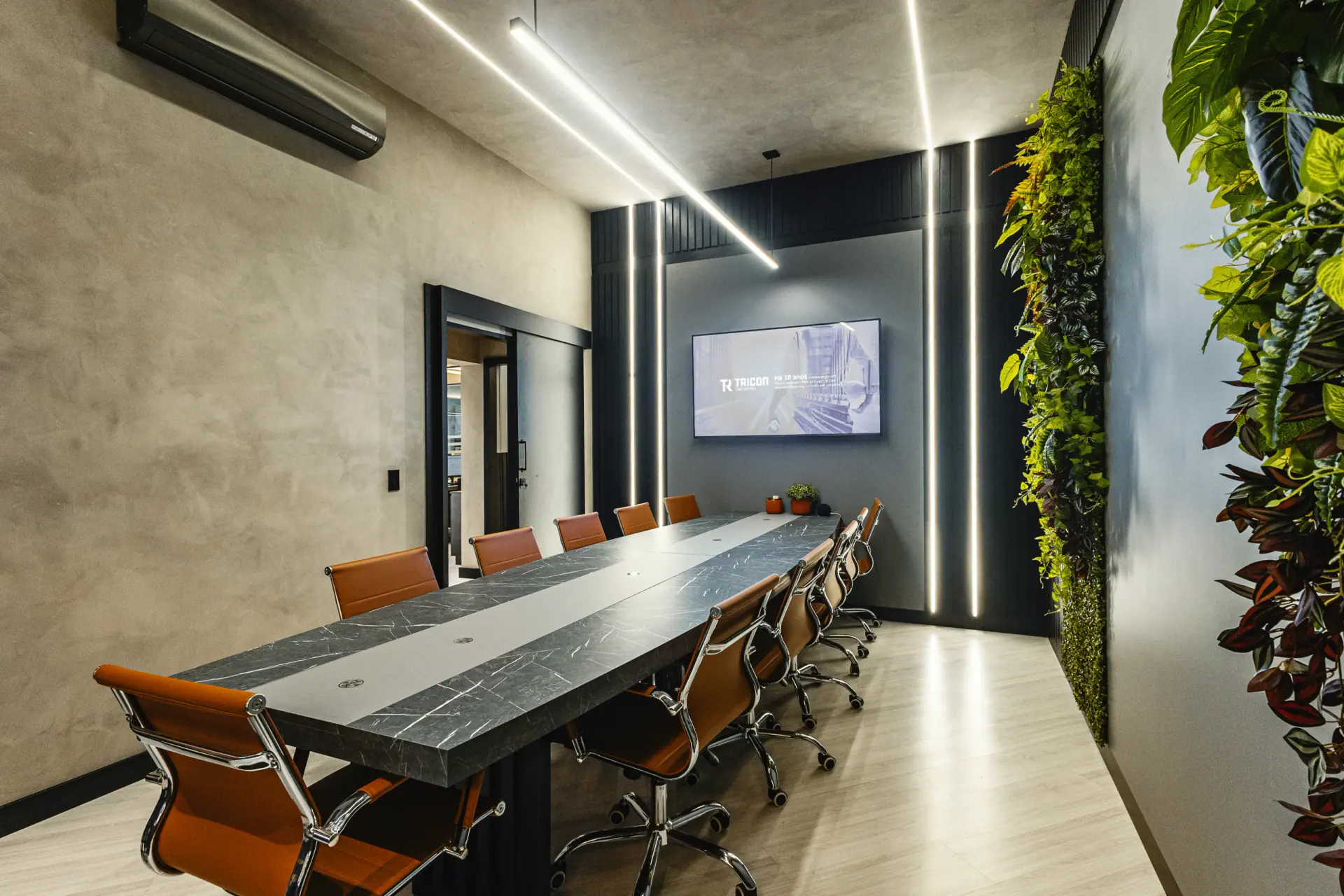 Sala de reuniões da sede Tricon, com mesa longa e jardim vertical